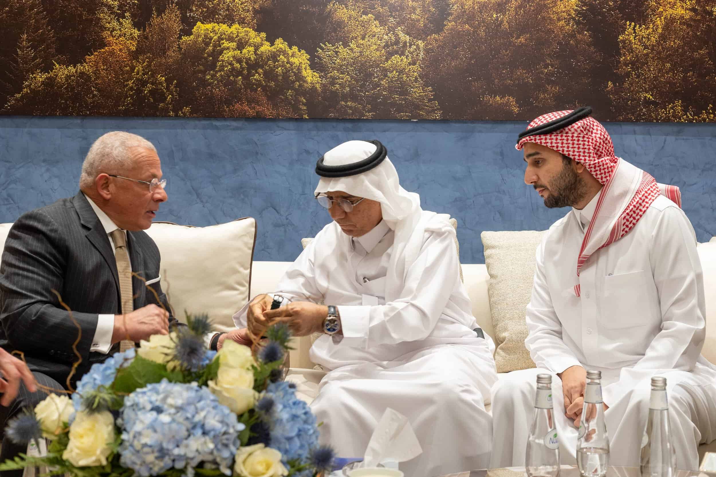 Elegant men in traditional attire discussing luxury timepieces at a formal event in Saudi Arabia.