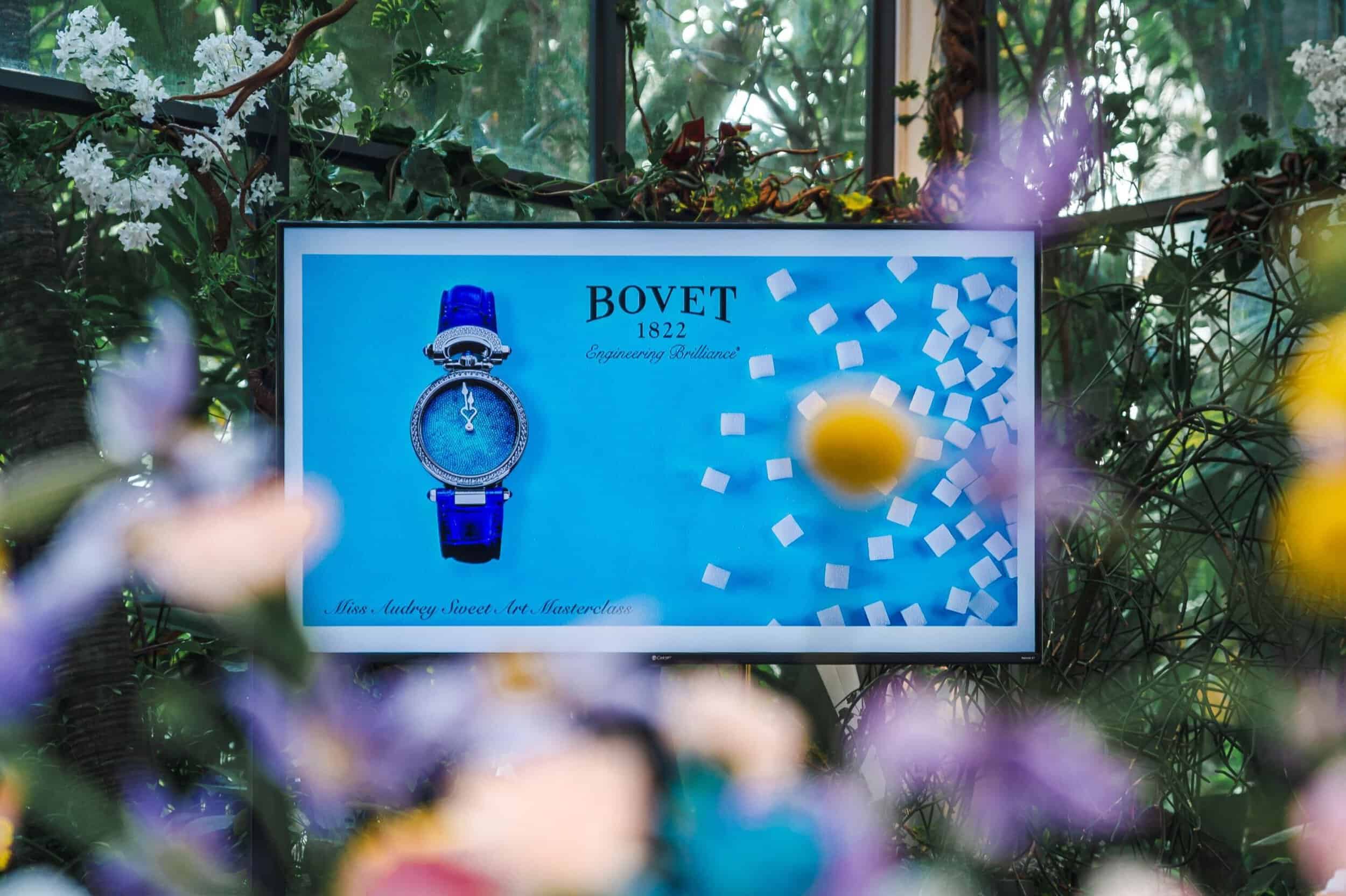 Elegant Bovet timepiece displayed on a digital screen amidst lush greenery and colorful flowers.