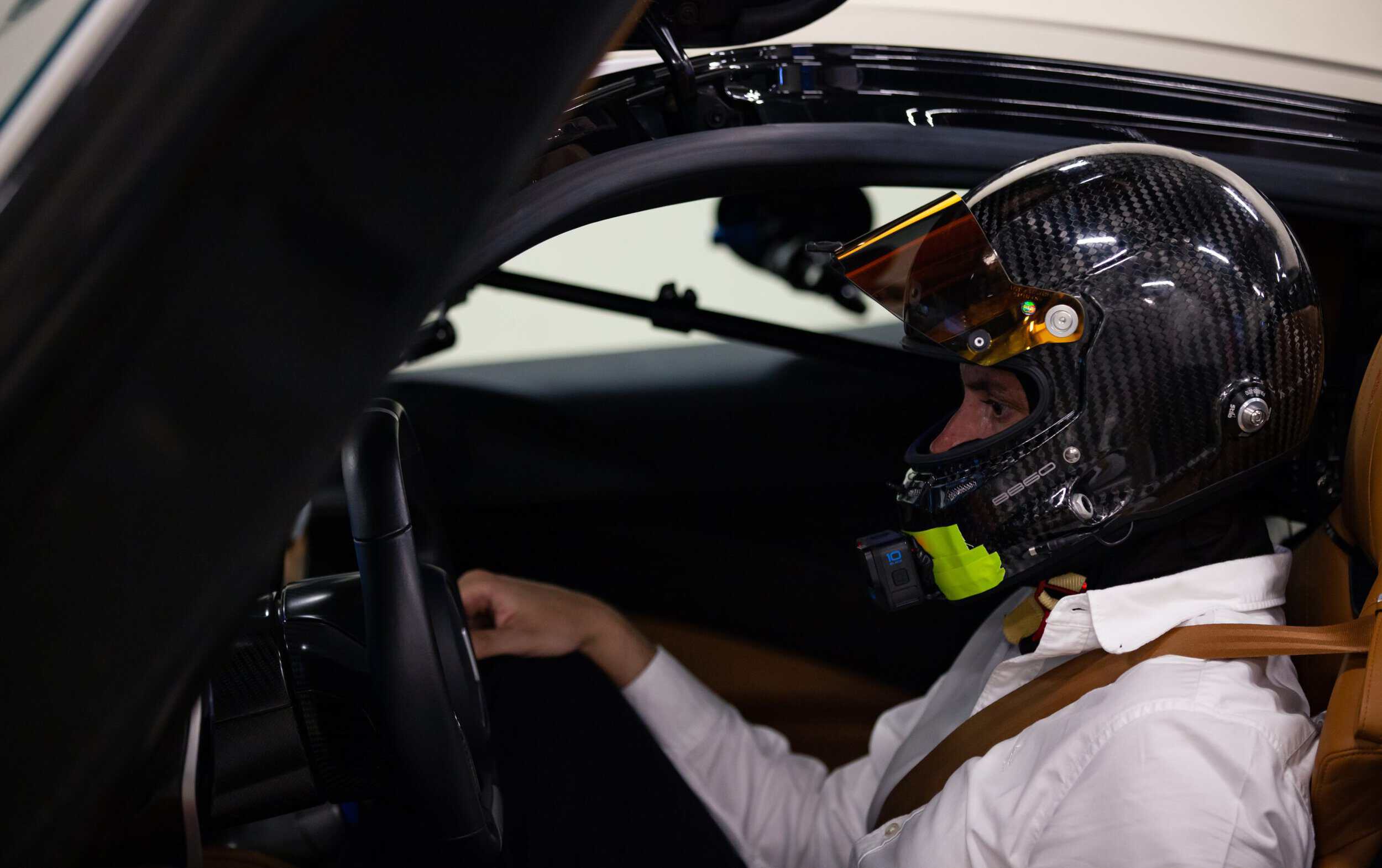 High-performance racing driver wearing a helmet inside a sports car cockpit.