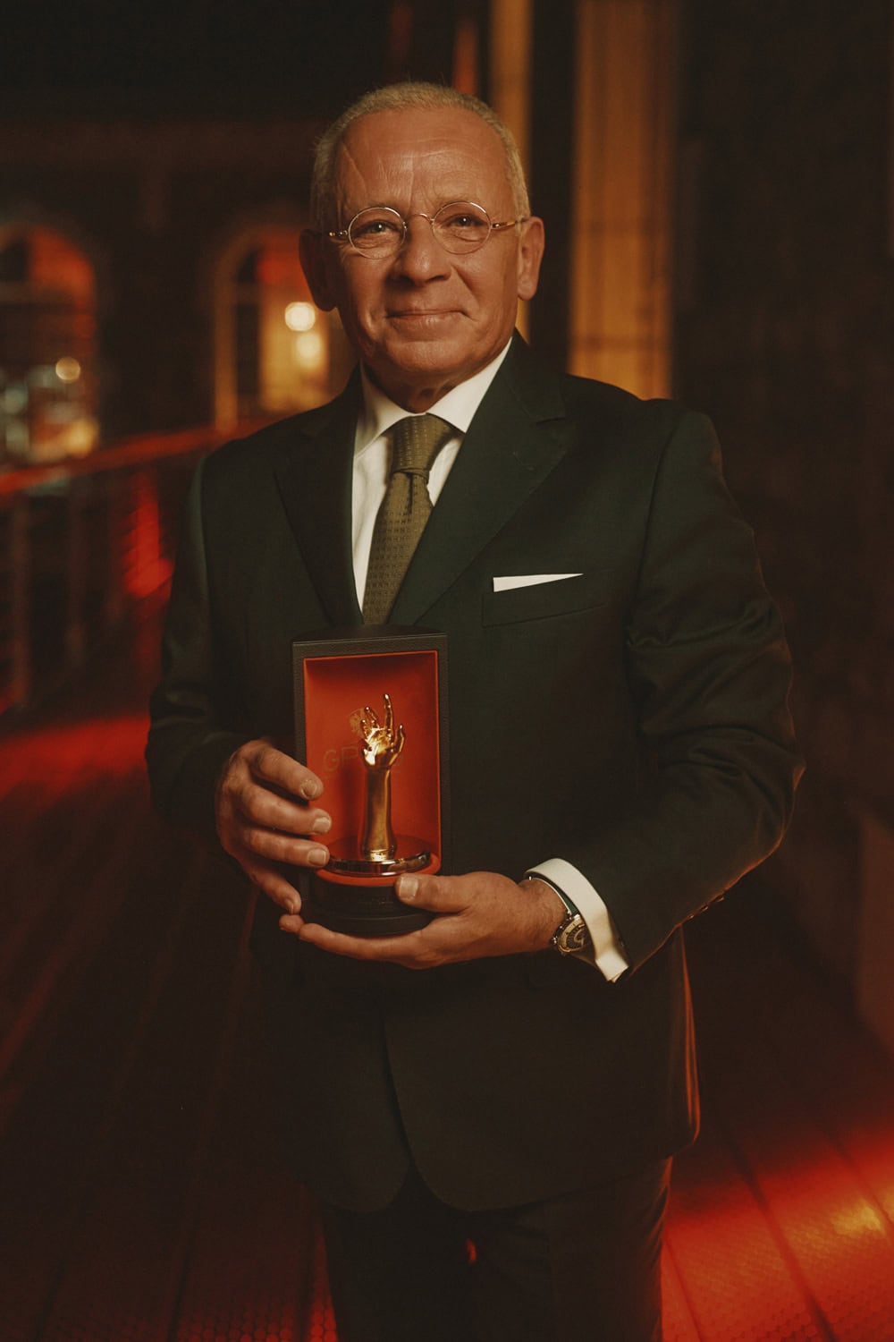 Distinguished man in formal suit holding Bovet watch award in elegant setting.